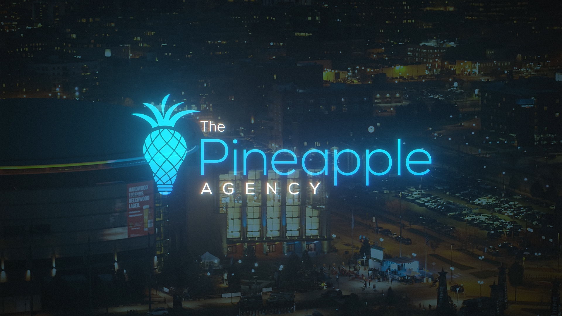 The Pineapple Agency logo with glowing blue pineapple design over blurred city nightscape background